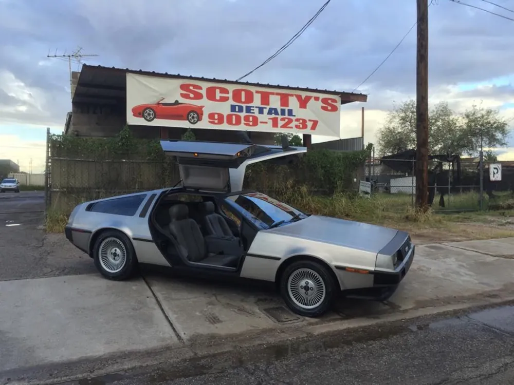 Silver DeLorean with gullwing doors open outside the shop